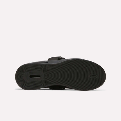 The image shows the bottom view of the Reebok Men's Legacy Lifter IV Shoes, featuring a black textured rubber sole with circular grip patterns for stability and a small rectangular cutout near the heel.
