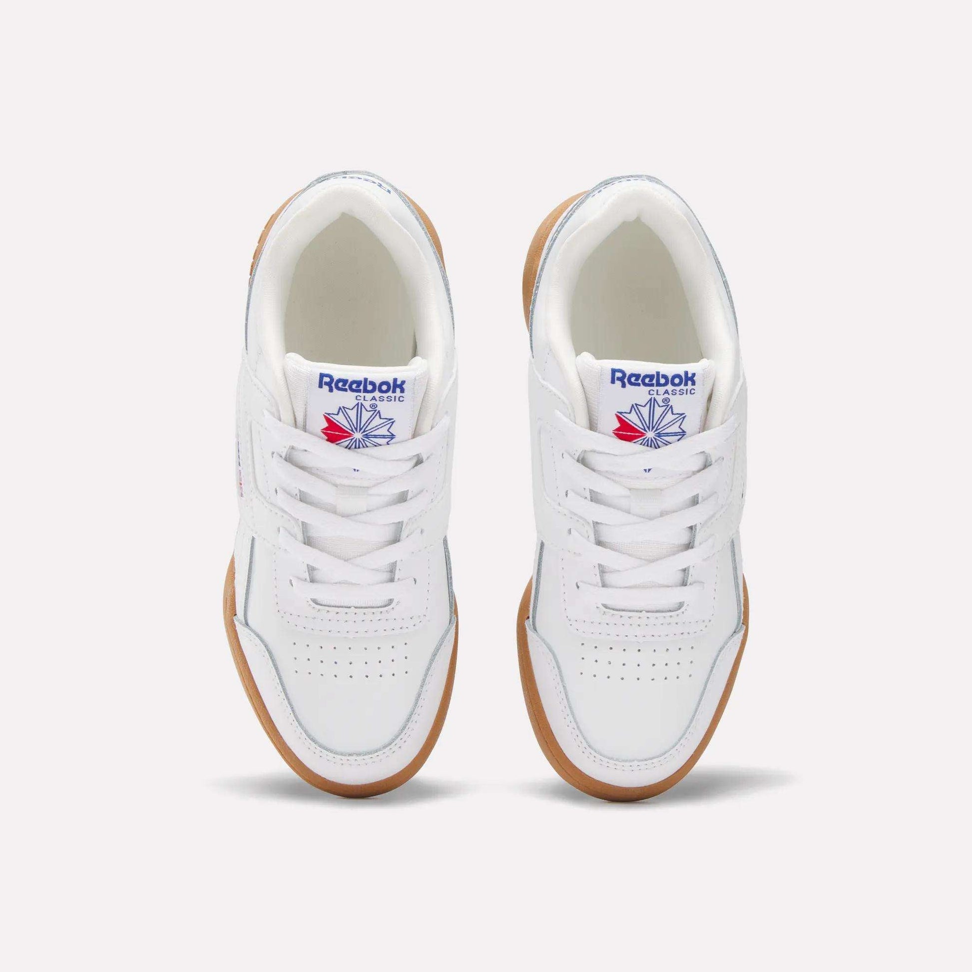 A pair of white Reebok Workout Plus Shoes for little kids, seen from above. They have gum soles, white laces, toe perforations, and display the blue and red Reebok logo on the tongue.