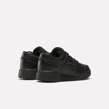 A pair of Reebok Workout Plus Shoes for little kids, shown in black from the back and side. These low-top sneakers feature laces and Reebok branding on the heel and side, displayed against a plain white background.