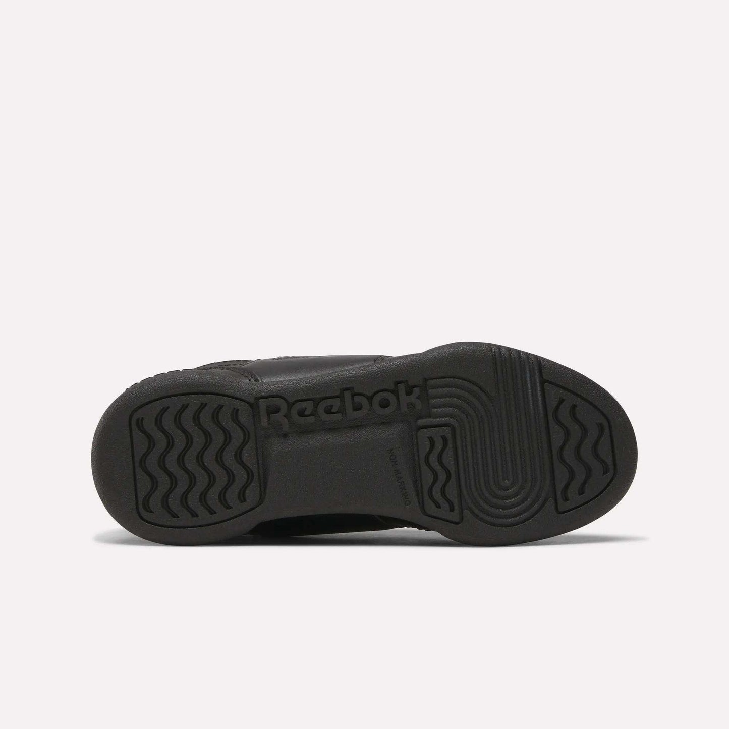 The image shows the black rubber sole of Reebok Workout Plus Shoes for little kids, viewed from the bottom, with wavy and straight tread patterns and the Reebok logo embossed in the center.
