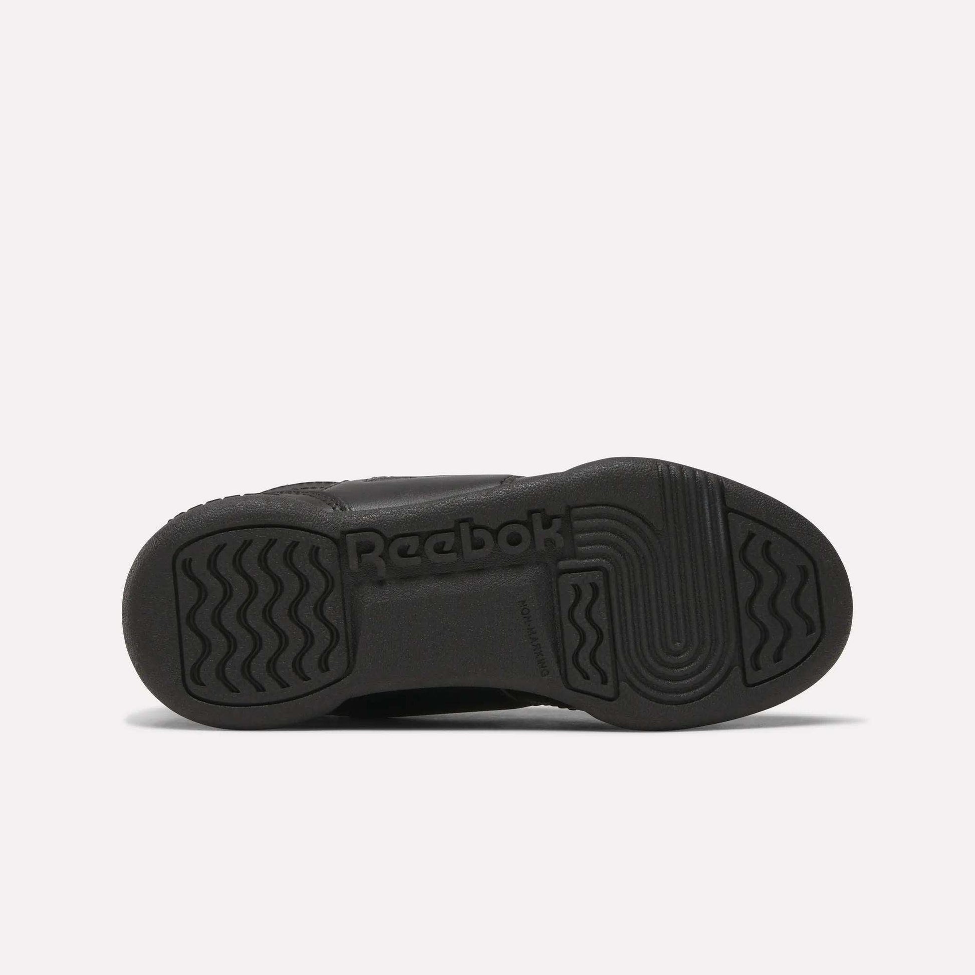 The image shows the black rubber sole of Reebok Workout Plus Shoes for little kids, viewed from the bottom, with wavy and straight tread patterns and the Reebok logo embossed in the center.