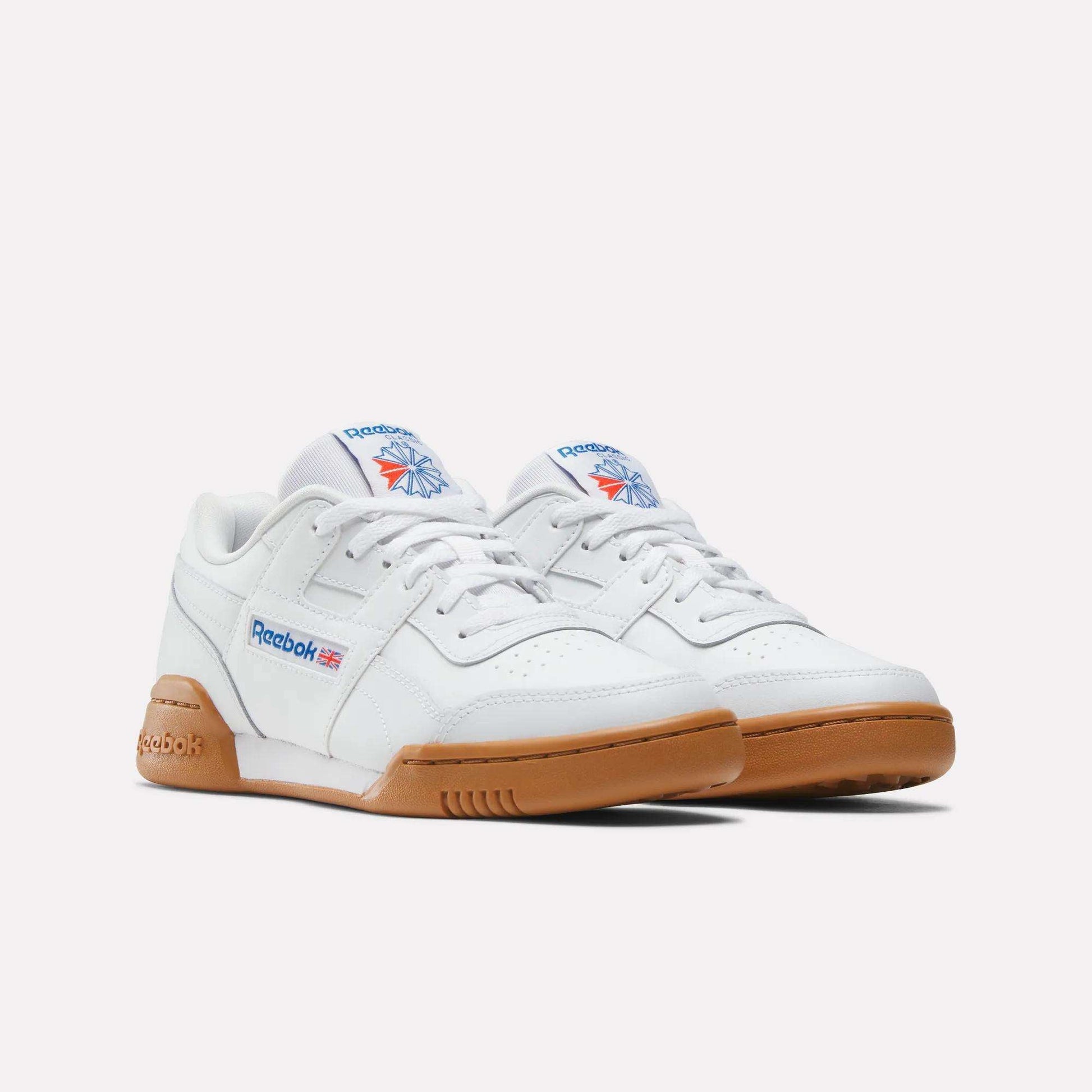 A pair of Reebok Workout Plus Shoes for big kids in white, with gum-colored soles and signature logos on the side and tongue, displayed against a plain white background.
