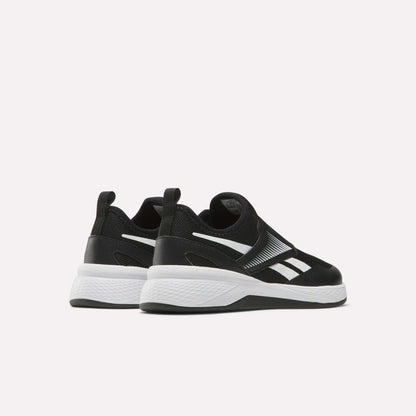 A pair of Reebok Nano Play Slip-On Shoes for little kids in black, with white soles and logo accents, shown facing away and slightly to the side on a plain light background.