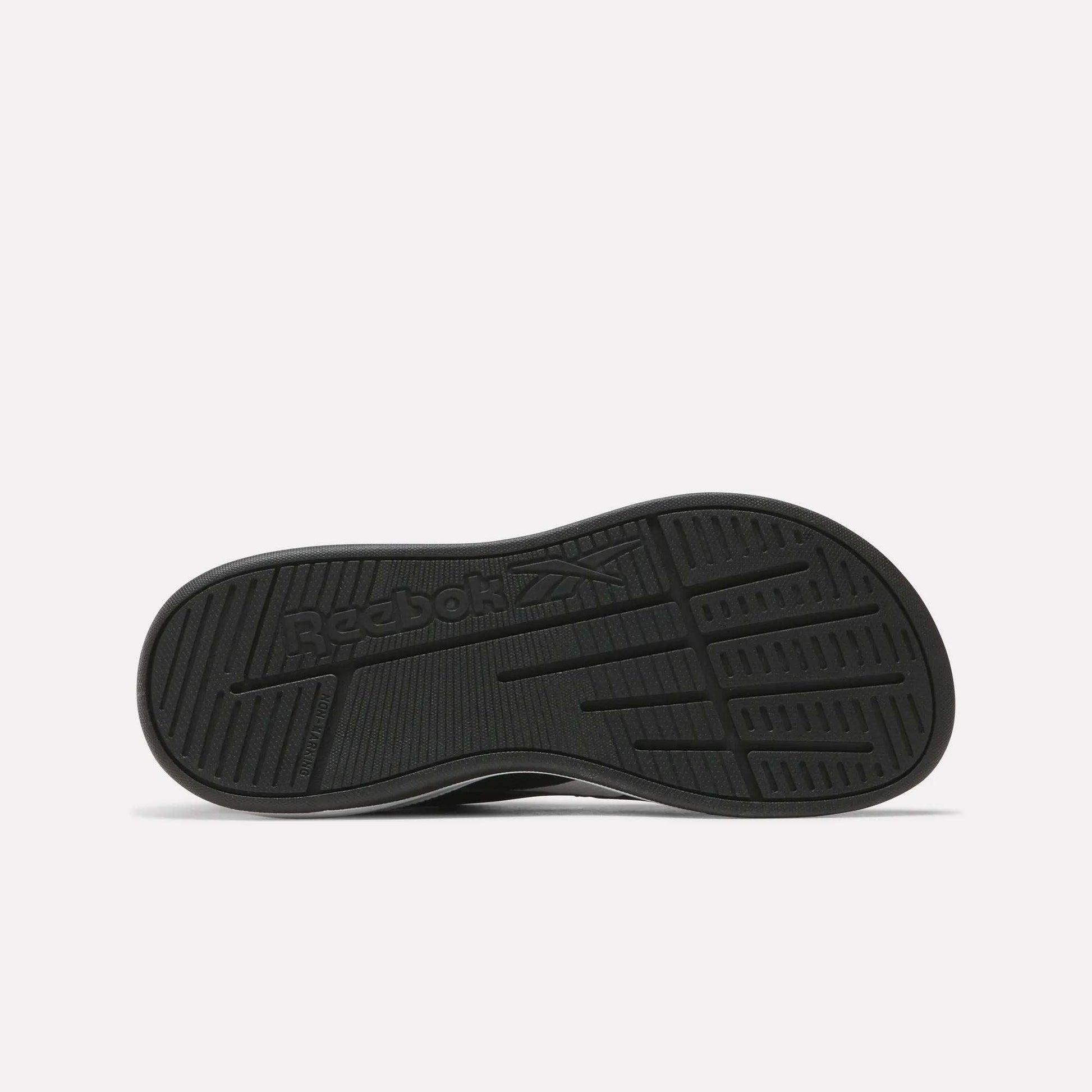 The Nano Play Slip-On Shoes for little kids by Reebok are shown from the bottom, featuring a black sole with the Reebok logo and textured tread for grip against a plain, light background that highlights these athletic shoes.