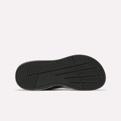 The Nano Play Slip-On Shoes for little kids by Reebok are shown from the bottom, featuring a black sole with the Reebok logo and textured tread for grip against a plain, light background that highlights these athletic shoes.