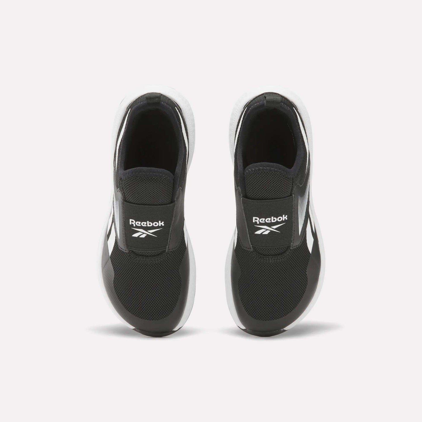 A pair of Reebok Nano Play Slip-On Shoes for little kids in black with white soles, seen from above. The shoes feature the Reebok logo on the tongue and are placed side by side on a plain white background.