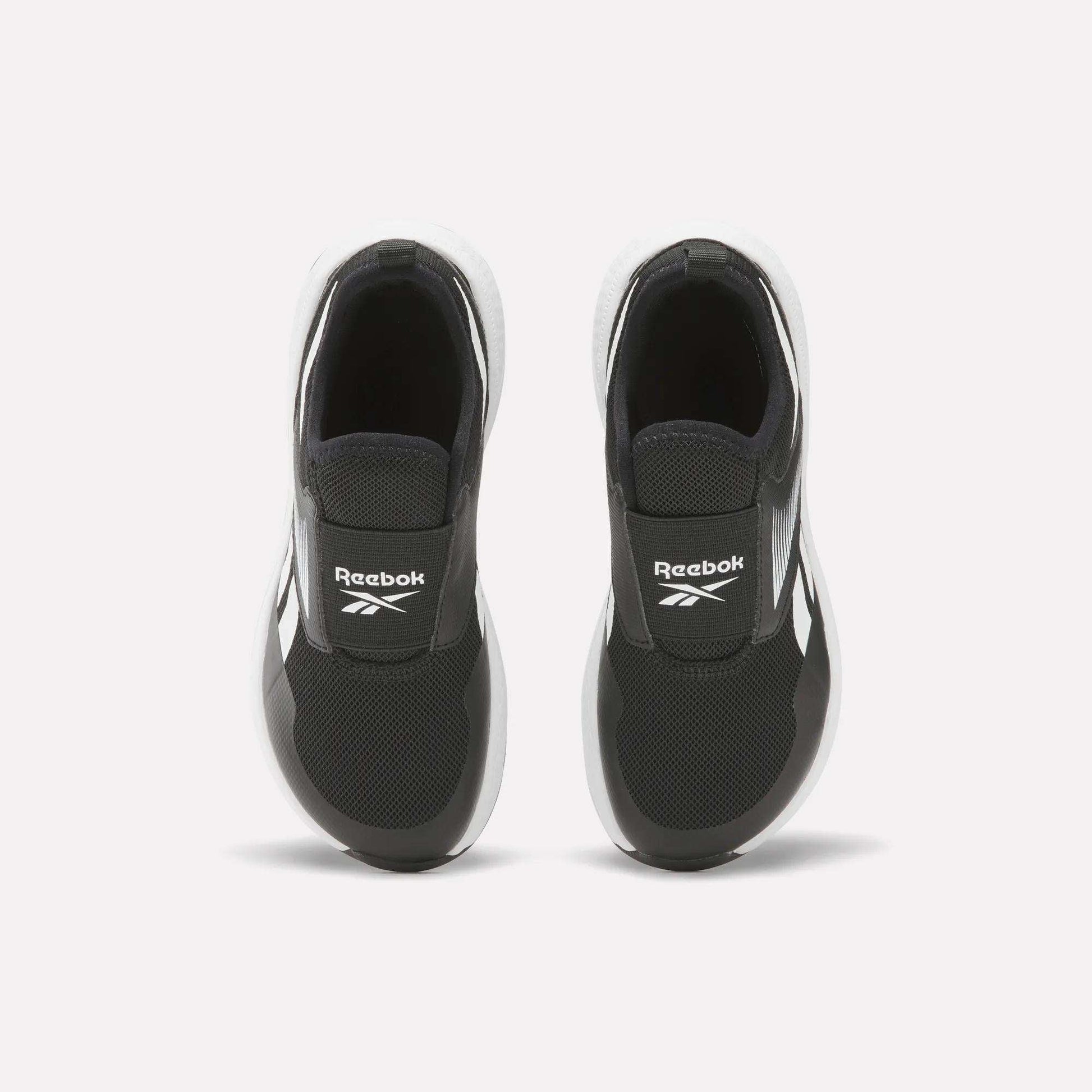 A pair of Reebok Nano Play Slip-On Shoes for little kids in black with white soles, seen from above. The shoes feature the Reebok logo on the tongue and are placed side by side on a plain white background.