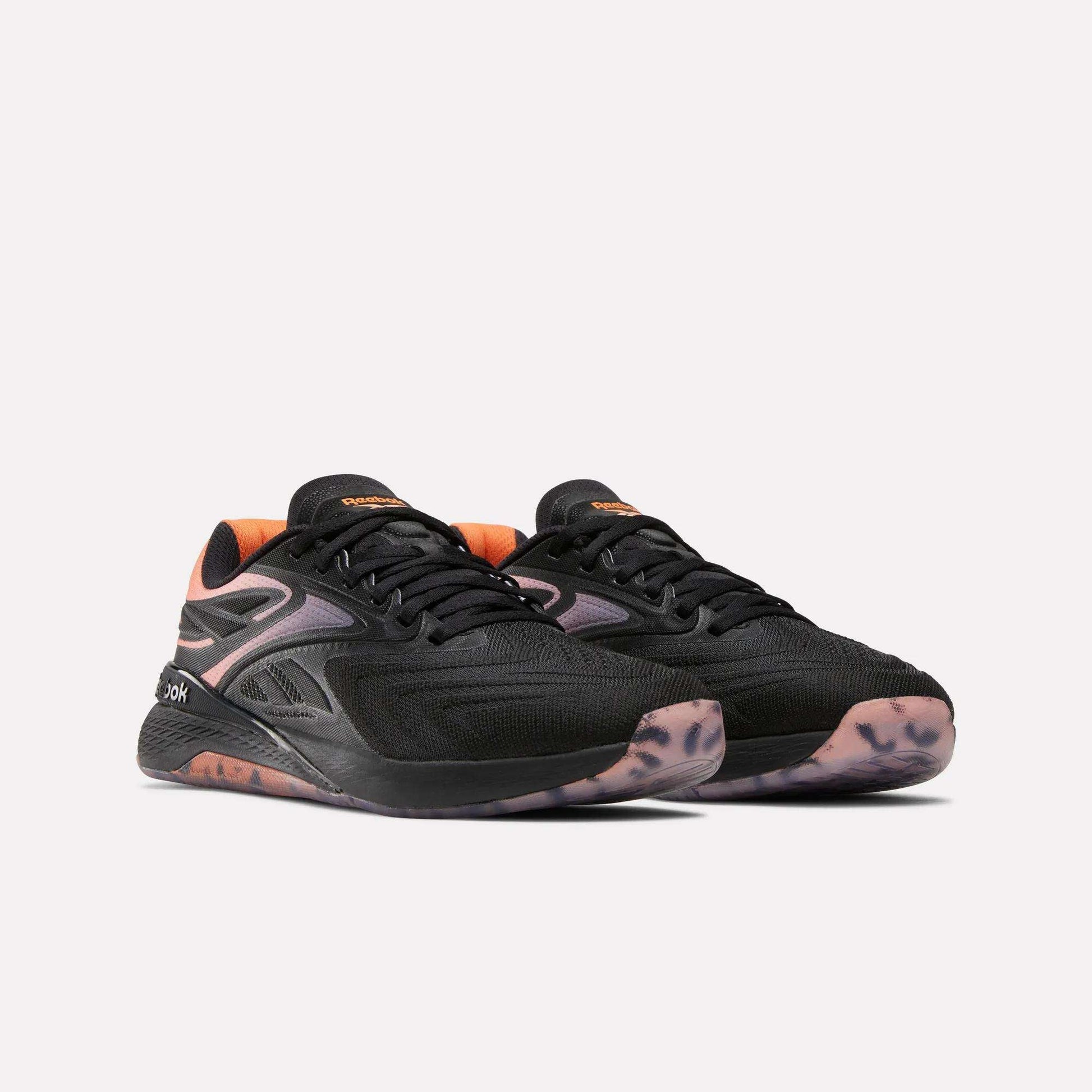 Women's Reebok Nano X5 Edge Training Shoes in black with orange accents, featuring mesh uppers and patterned translucent rubber soles, shown against a plain light background.