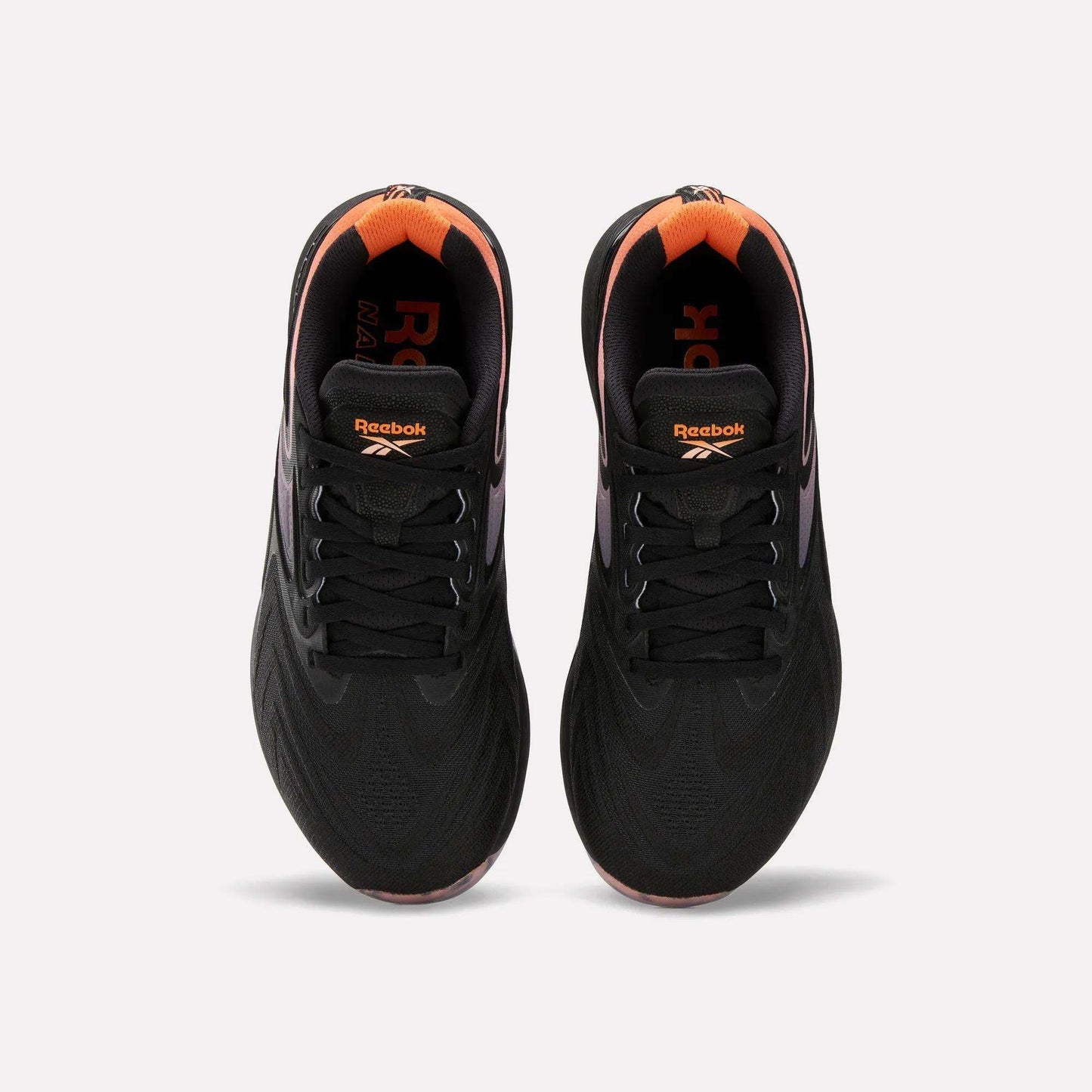 Top view of Women's Nano X5 Edge Training Shoes by Reebok in black with orange heel and inner accents, Reebok logo on tongue and insole. Shoes shown side by side on a white background.