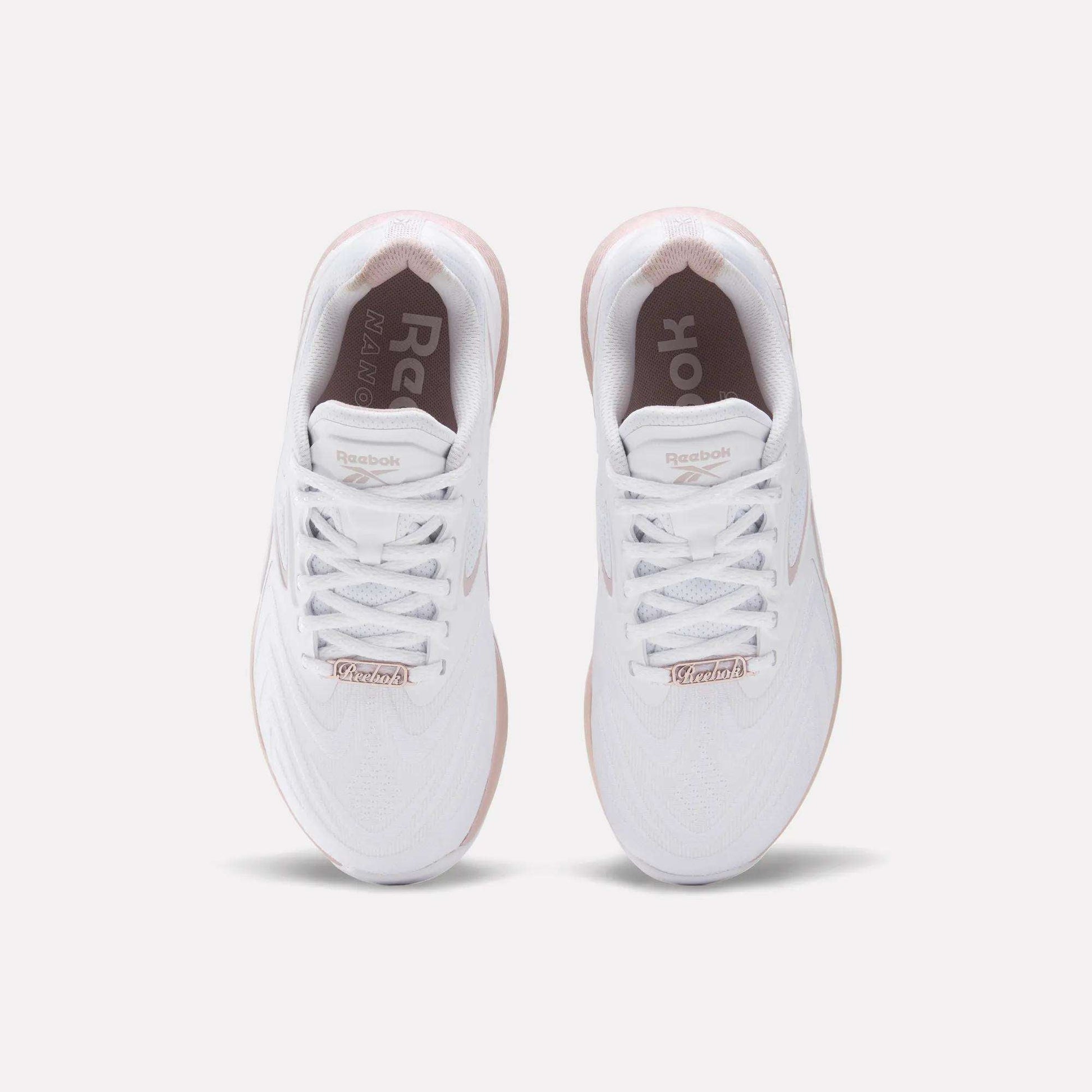 The Reebok Women's Nano X5 Edge Training Shoes feature a white upper, white laces, and a light pink sole. The Reebok logo appears on the insoles and tongue, combining style and performance—ideal for HIIT workouts.