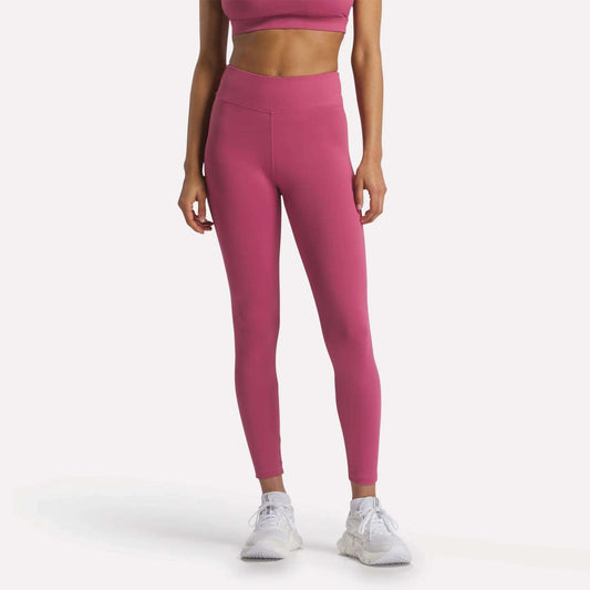 A woman models Reebok Women's Lux-Lite High-Rise Tights and a matching pink sports bra, both crafted from RBK-DRY fabric, with white athletic shoes. She stands against a plain white background, head not shown.