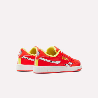 The Reebok x Paw Patrol Club C Revenge Shoes for little kids feature vibrant red and yellow colors, white soles, black spotted accents, and the Reebok logo inspired by retro tennis style, displayed against a plain light background.
