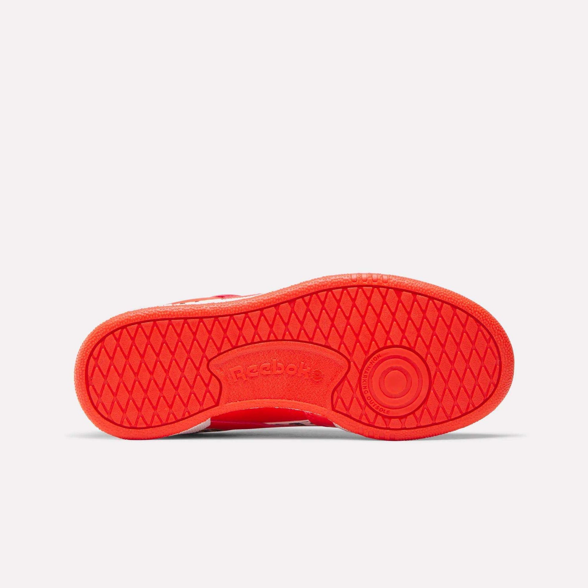 The image shows the sole of a red Reebok x Paw Patrol Club C Revenge Shoe for little kids, featuring a diamond textured pattern, Reebok branding in the center, and a circular heel design for comfort.