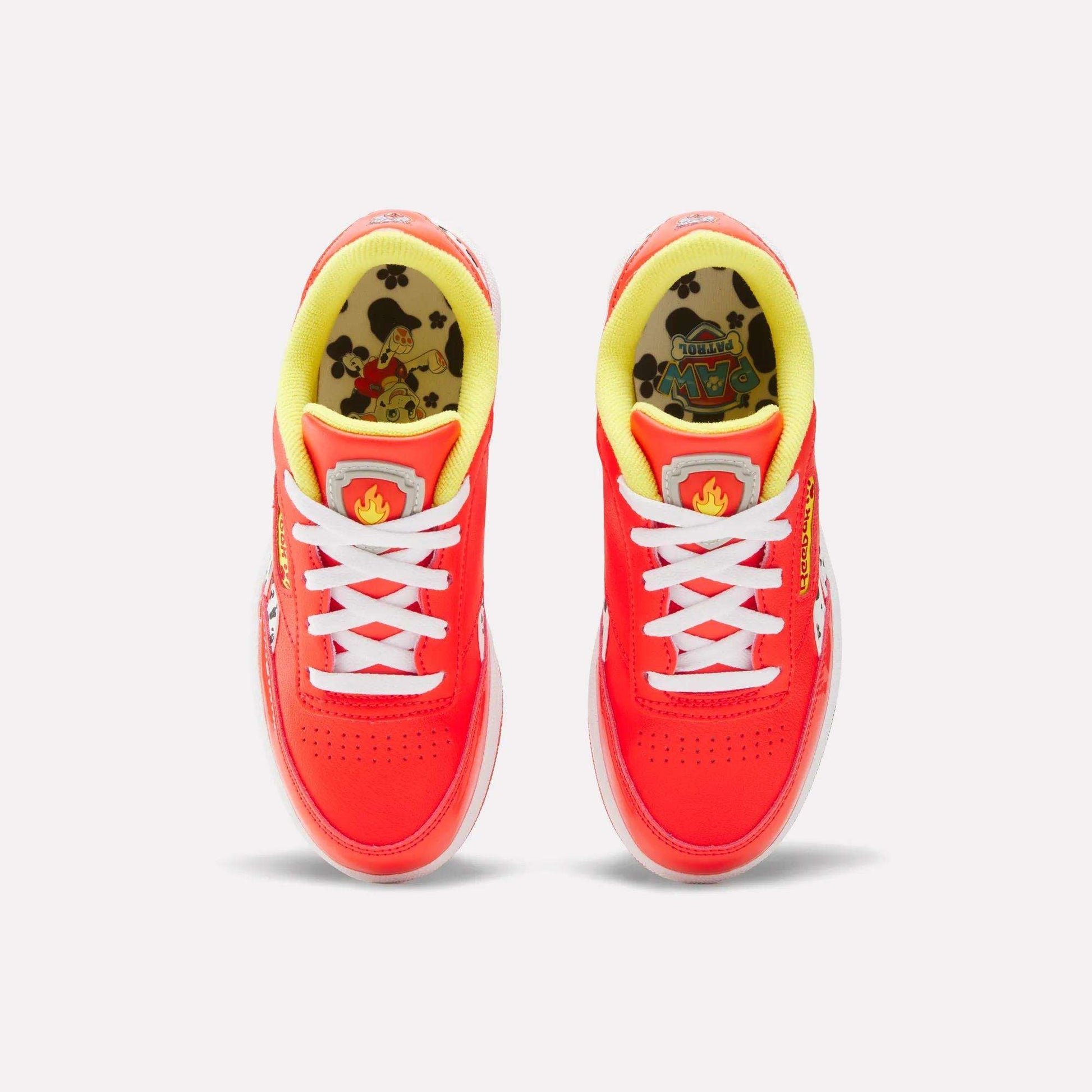 Top view of Reebok x Paw Patrol Club C Revenge Shoes for little kids, featuring a vibrant red color, white laces, yellow lining, cartoon Paw Patrol insoles, retro tennis style, and playful flame detail on the tongue.