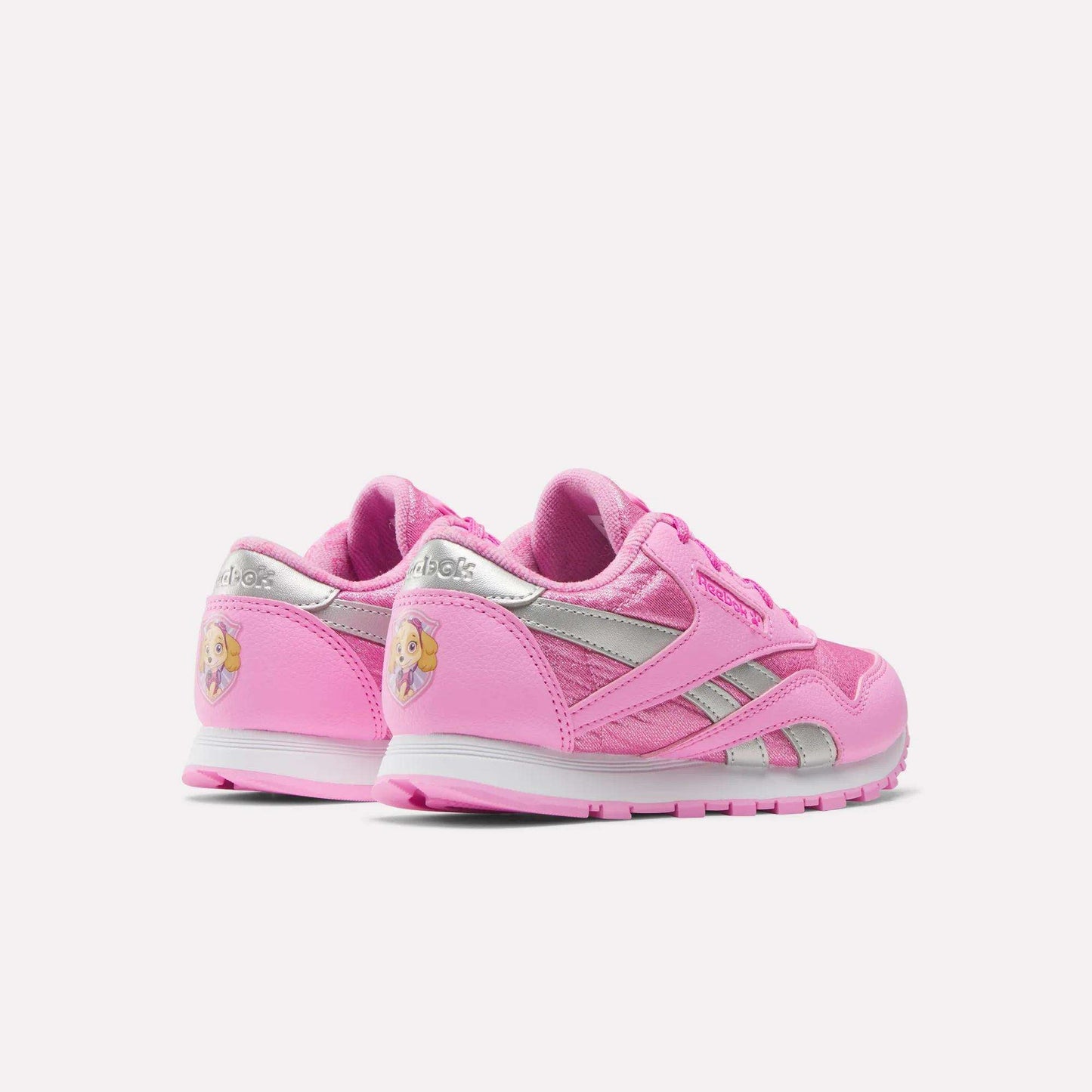 Two pink Reebok x Paw Patrol Classic Nylon Shoes for little kids, featuring silver accents and a blonde princess graphic on the heel. Made from suede for comfort. Shown on a plain white background.
