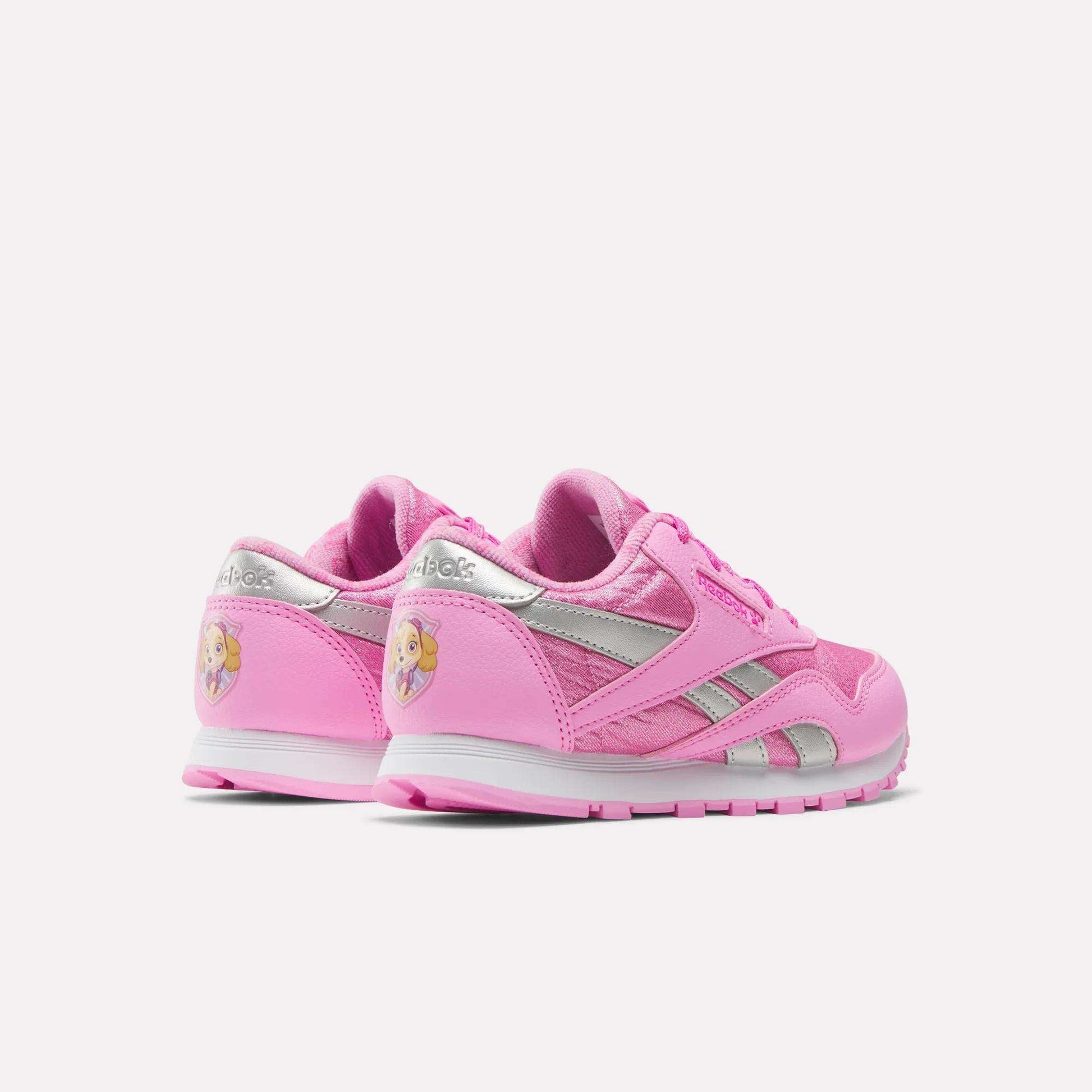 Two pink Reebok x Paw Patrol Classic Nylon Shoes for little kids, featuring silver accents and a blonde princess graphic on the heel. Made from suede for comfort. Shown on a plain white background.