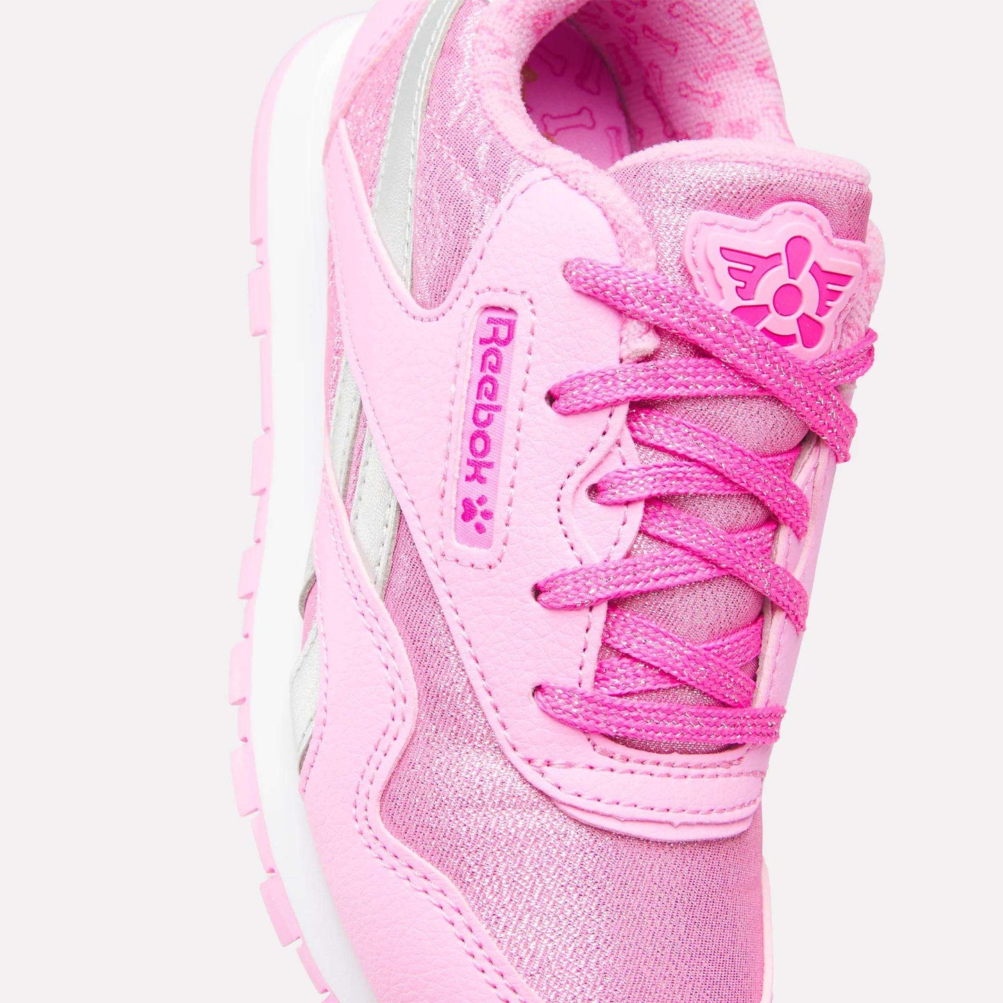 A close-up of the Reebok x Paw Patrol Classic Nylon Shoes for little kids, featuring bright pink laces, a silver stripe, pink Reebok logos, a white sole, suede accents, and a playful design for comfy everyday wear.