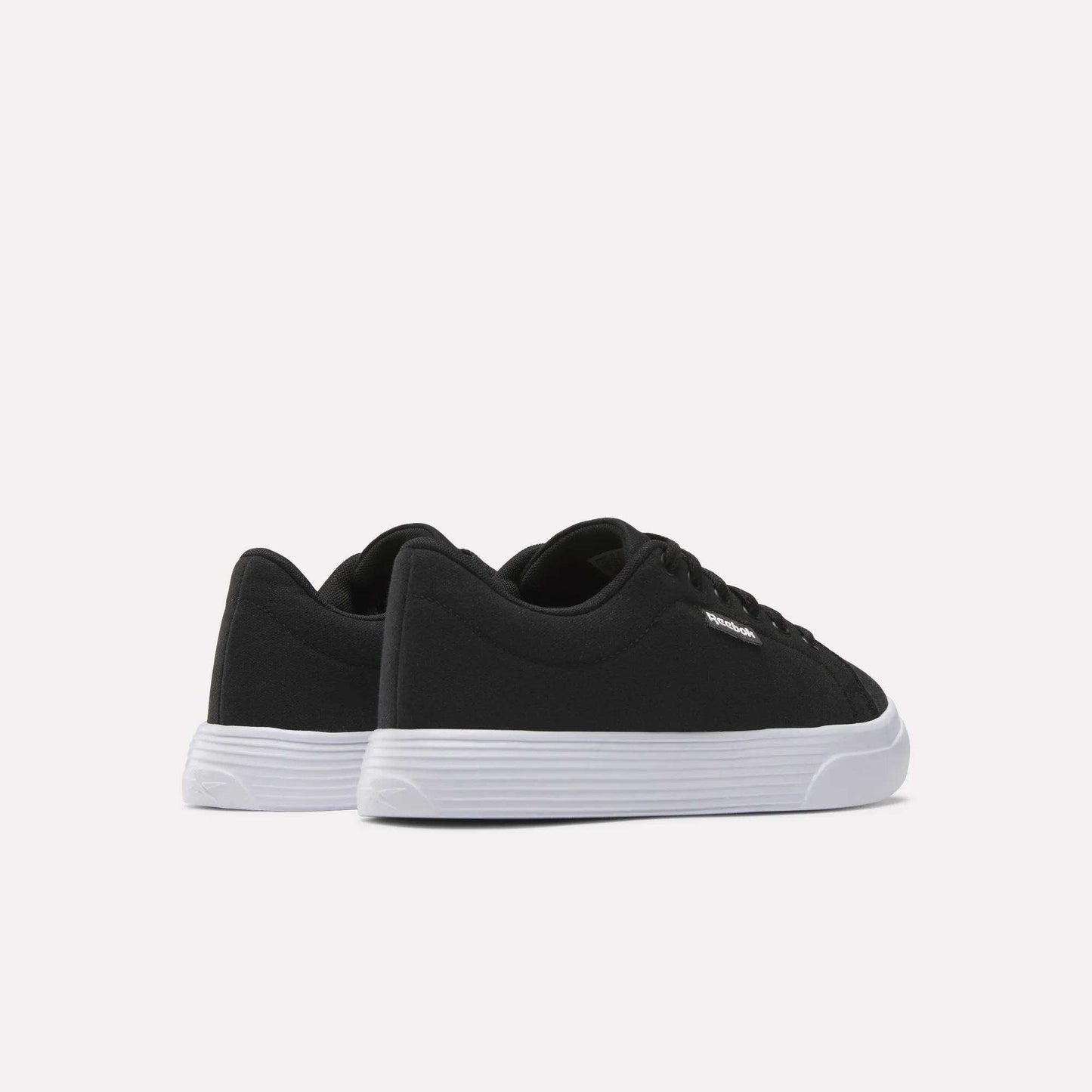 The Women's OnLux Court Lite Walking Shoes by Reebok are black low-top, comfortable walking shoes with white rubber soles, displayed from the back and side on a plain white background.