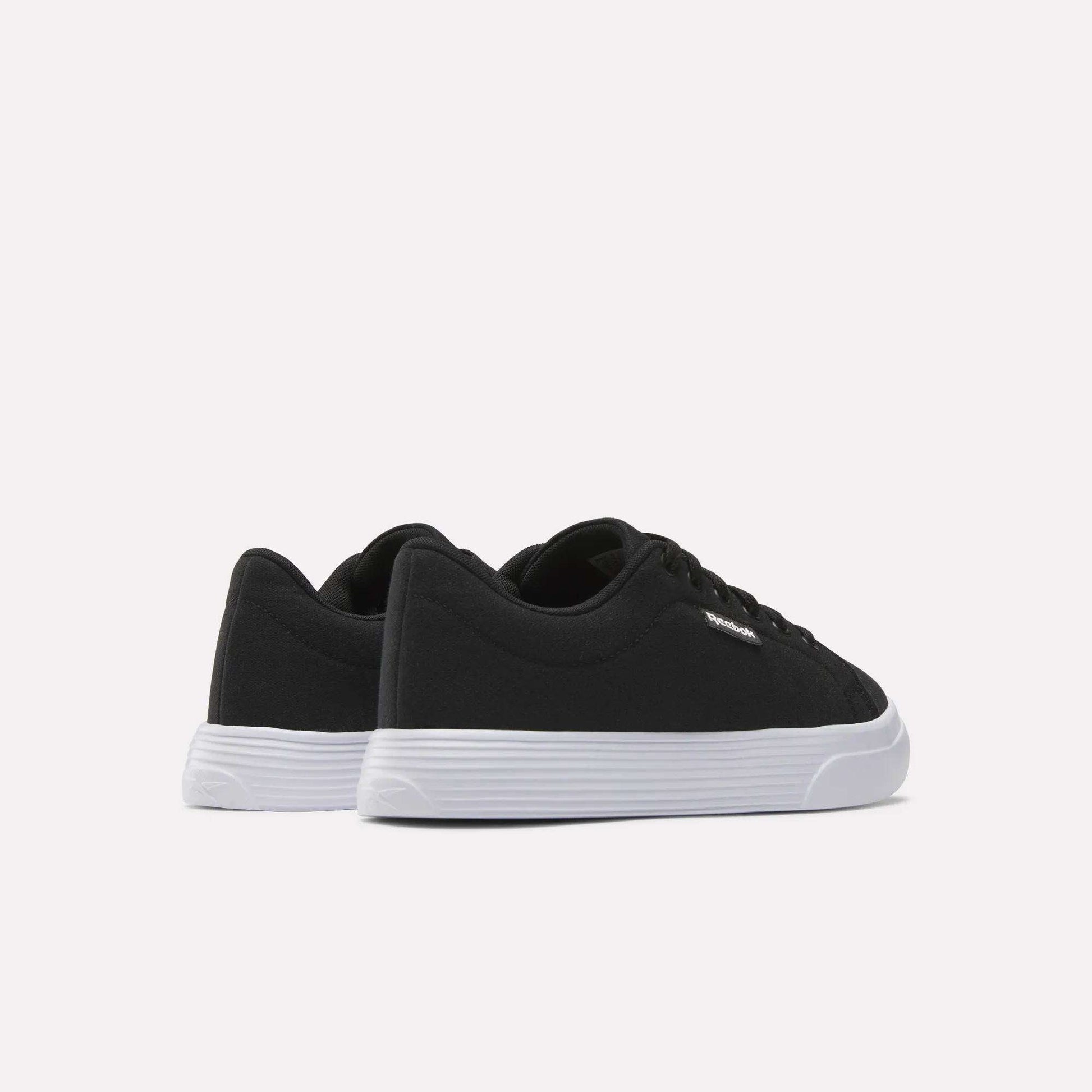 The Women's OnLux Court Lite Walking Shoes by Reebok are black low-top, comfortable walking shoes with white rubber soles, displayed from the back and side on a plain white background.