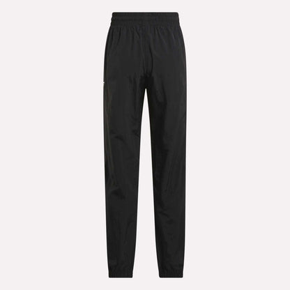 Women's Vector Track Pants by Reebok, shown in black on a plain light background. These feature an elastic waistband and cuffs, straight-leg fit, and lightweight shiny material for a retro-inspired look.