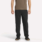A person wearing a brown short-sleeve shirt, Reebok Men's Train Woven Unlined Pants, and black sneakers stands facing forward against a plain white background.