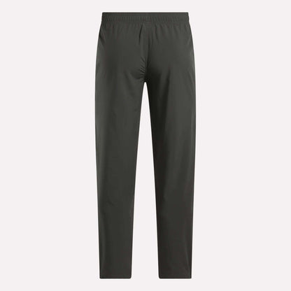 Reebok Men's Train Woven Unlined Pants in dark gray feature a straight-leg design and elastic waistband, ideal as lightweight workout or gym pants. Shown against a light background.