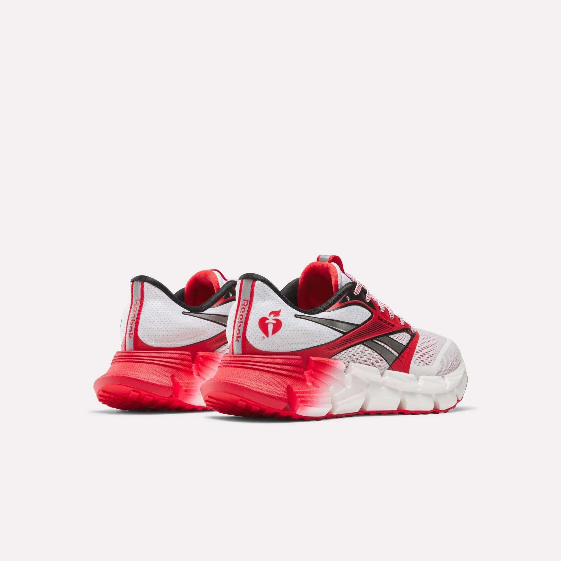 The Reebok Women's FloatZig 2 AHA Running Shoes feature a white design with red and black accents, a heart logo on the heel, red gradient sole, and energy-returning cushioning, displayed on a plain light background.