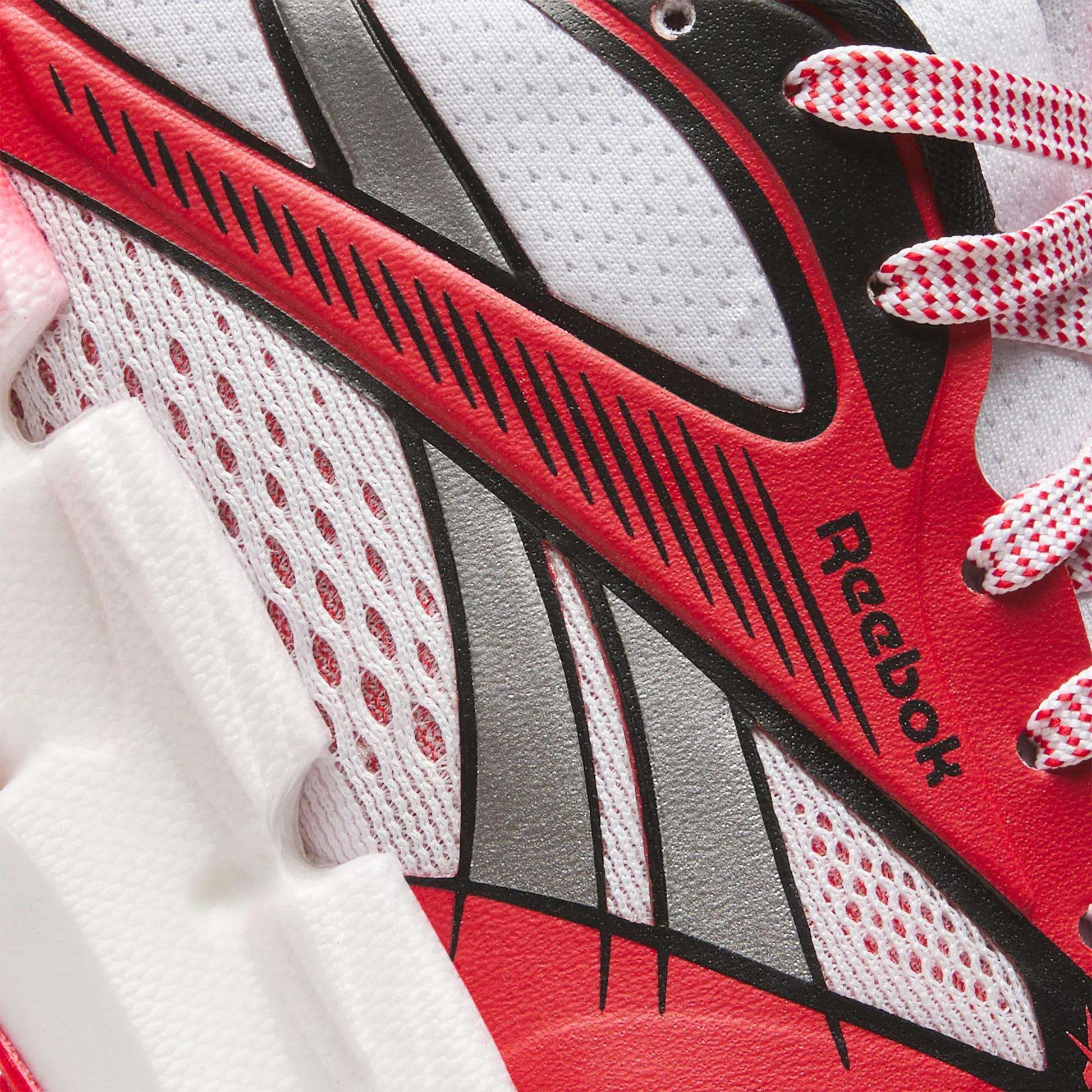 Close-up of a Reebok Women's FloatZig 2 AHA Running Shoe in red, white, and black, featuring textured mesh, bold graphic lines, energy-return cushioning foam midsole, and Reebok branding by the laces.