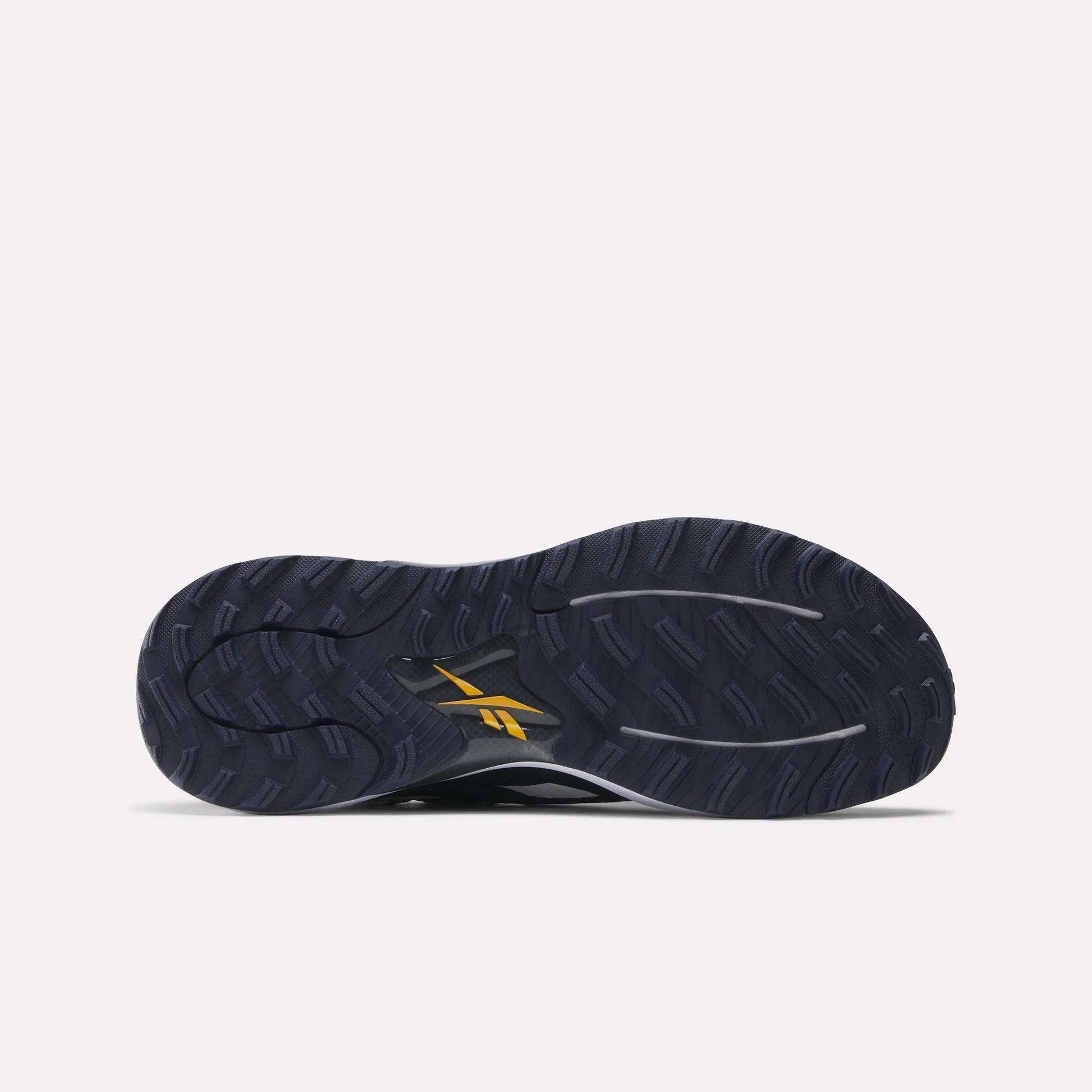 The image shows the bottom of a dark navy Nano Golf Shoe by Reebok with a textured tread, a yellow Reebok logo near the sole’s center, and Floatride performance foam for enhanced comfort.