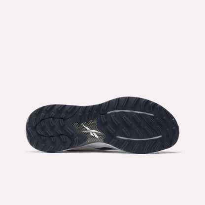The image shows the dark blue, textured rubber outsole of Reebok Nano Golf Shoes with deep grooves for traction and a white Reebok logo in the center. This pairs with a lightweight FlexWeave upper for support and comfort, set against a light gray background.