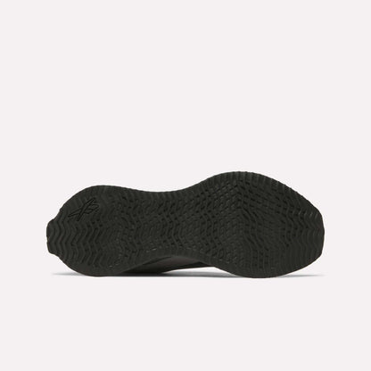 The image shows the black, textured rubber outsole of the Reebok Zig Dynamica STR Shoes, viewed from the bottom. It features a wave-like tread pattern, a small logo on the left side, and a plain, light-colored background.