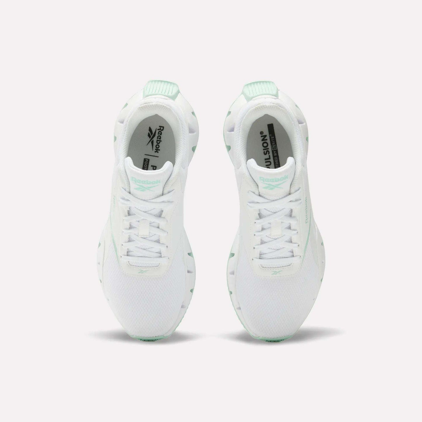 A pair of Reebok Women's Zig Dynamica STR Shoes in white with mint green accents, featuring breathable mesh for comfort, shown from above on a plain white background.