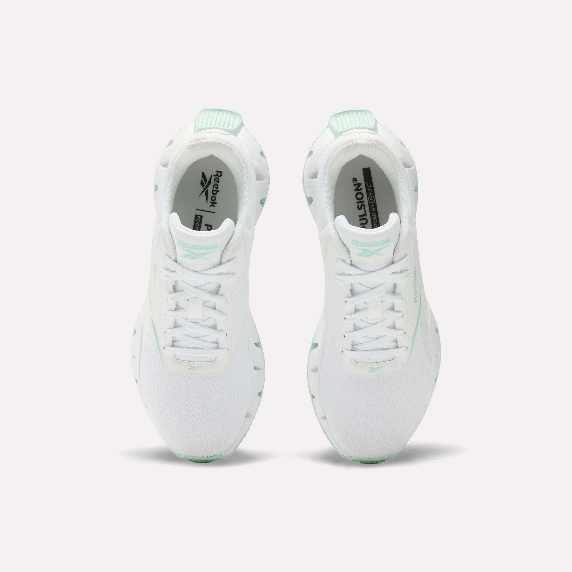 A pair of Reebok Women's Zig Dynamica STR Shoes in white with mint green accents, featuring breathable mesh for comfort, shown from above on a plain white background.