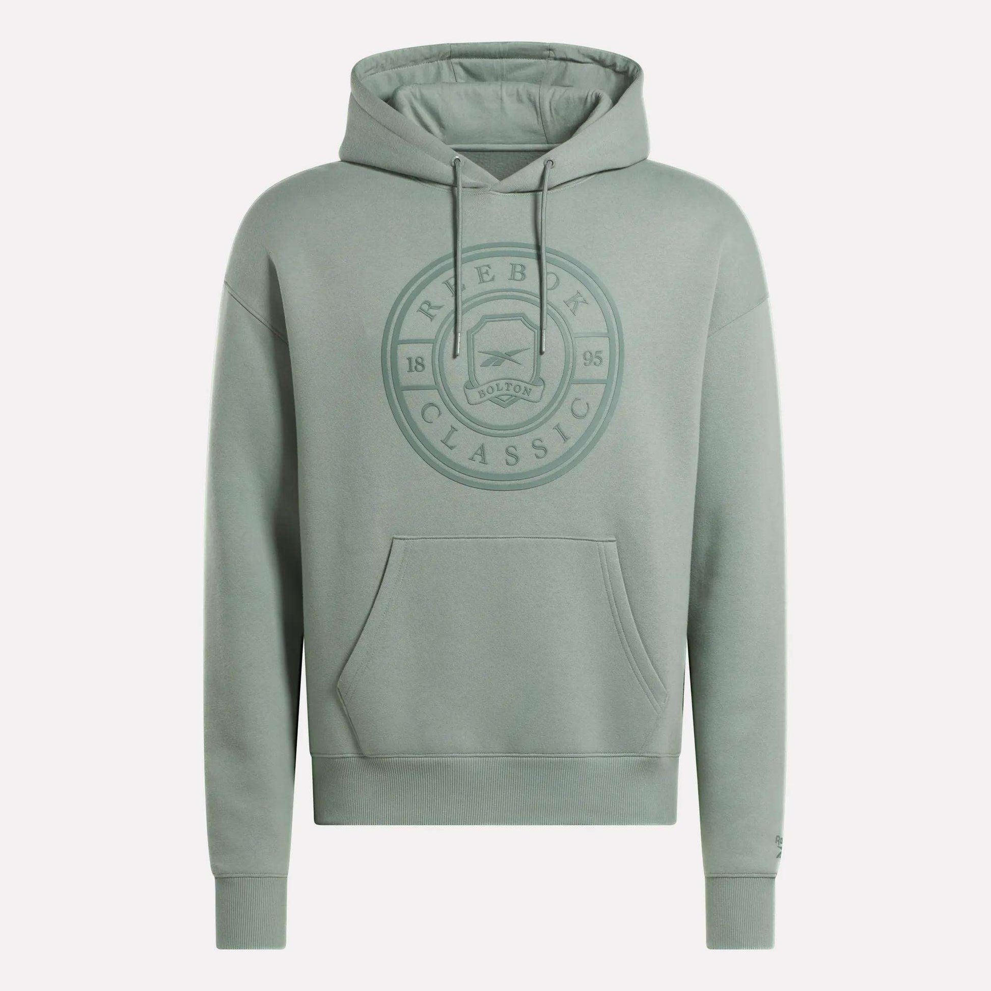 The Men's Crest Hoodie by Reebok is a light green soft fleece hoodie with a relaxed fit, front pocket, drawstring hood, and an embossed circular chest logo reading "Reebok Classic 1895 Bolton." Finished with long sleeves.