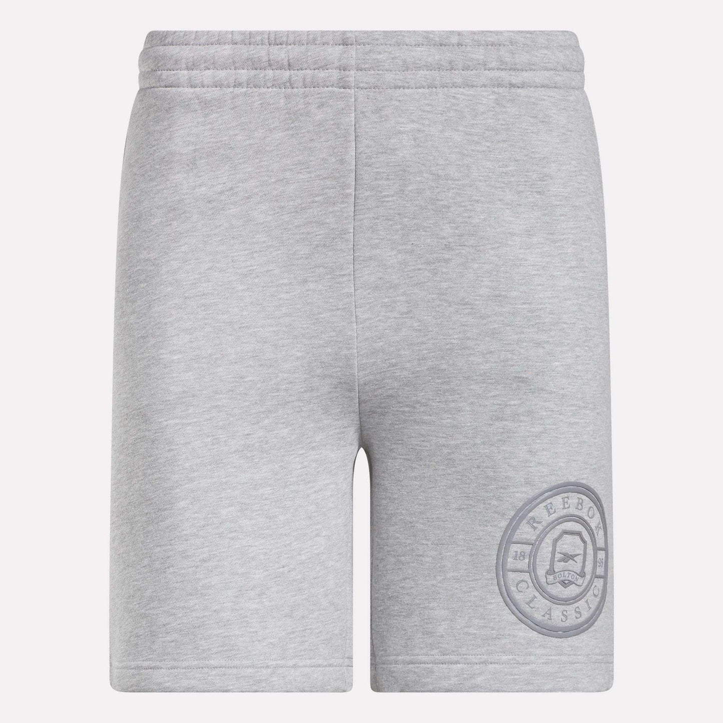Reebok Men's Crest Shorts in light grey feature an elastic waistband and relaxed fit. Made from cotton, these shorts have a simple design without visible pockets or drawstrings and display a circular Reebok Classic logo on the lower left leg.