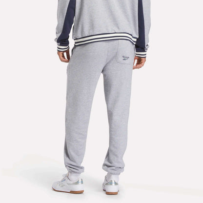 A person is shown from the back wearing Reebok Men's Lawn Club French Terry Jogger Pants, a grey tracksuit with navy sleeve stripes and a small logo on the right pocket, paired with white sneakers.