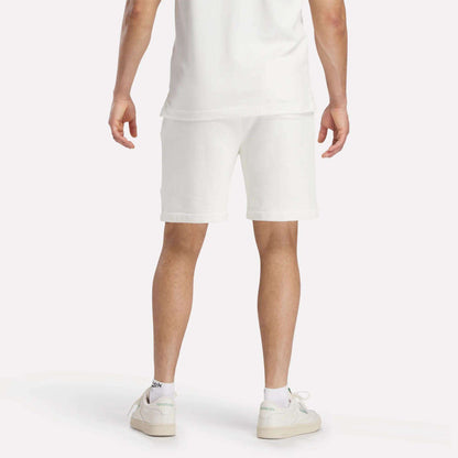 A person in a white t-shirt, Reebok Men's Lawn Club Shorts, and white sneakers stands with their back to the camera against a plain white background.