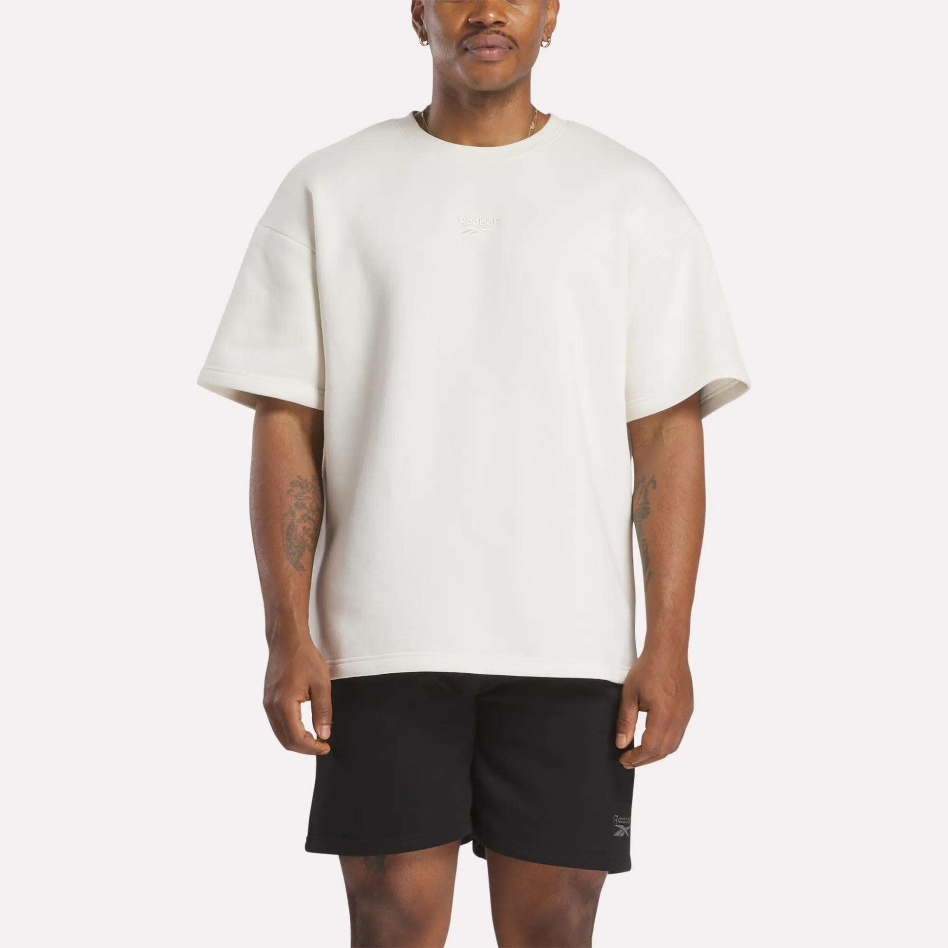 A man in a white, relaxed fit Reebok Men's Wardrobe Essentials T-Shirt.