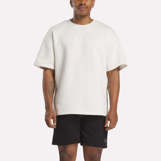 A man in a white, relaxed fit Reebok Men's Wardrobe Essentials T-Shirt.