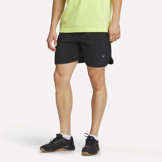 A person in a light green shirt, black Reebok Men's Run Shorts with inner tights, black athletic shoes, and white socks stands against a plain white background. The person's head is not visible in the image.