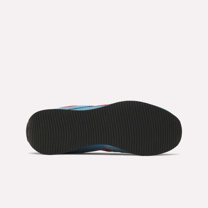 The image shows the bottom view of Reebok R100 Shoes with a black, textured rubber sole. Hints of blue and red on the upper echo '70s running style, while the plain white background highlights these low-profile sneakers.