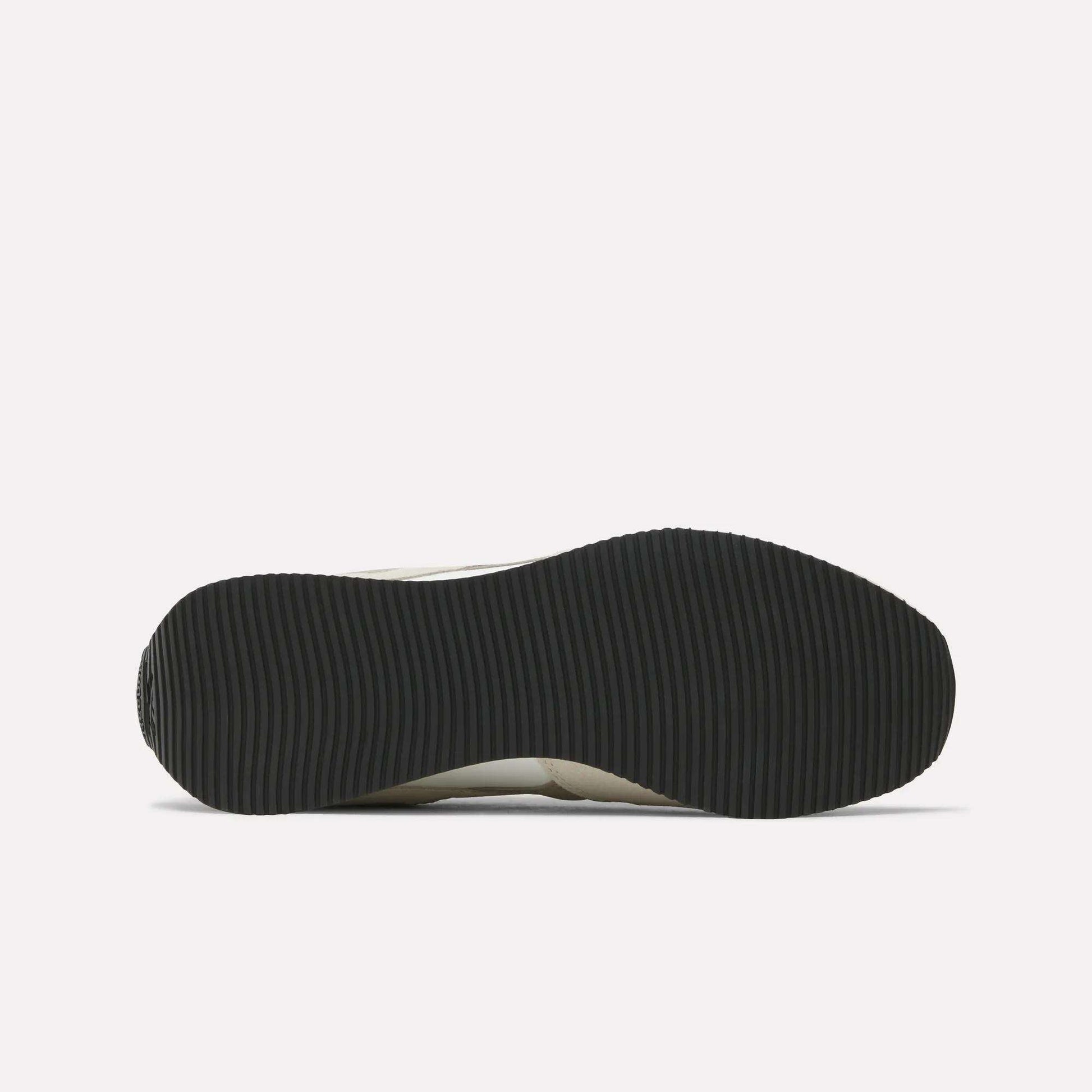 The image shows the black, ribbed outsole of Reebok R100 Shoes viewed from below on a white background, evoking classic '70s running style.