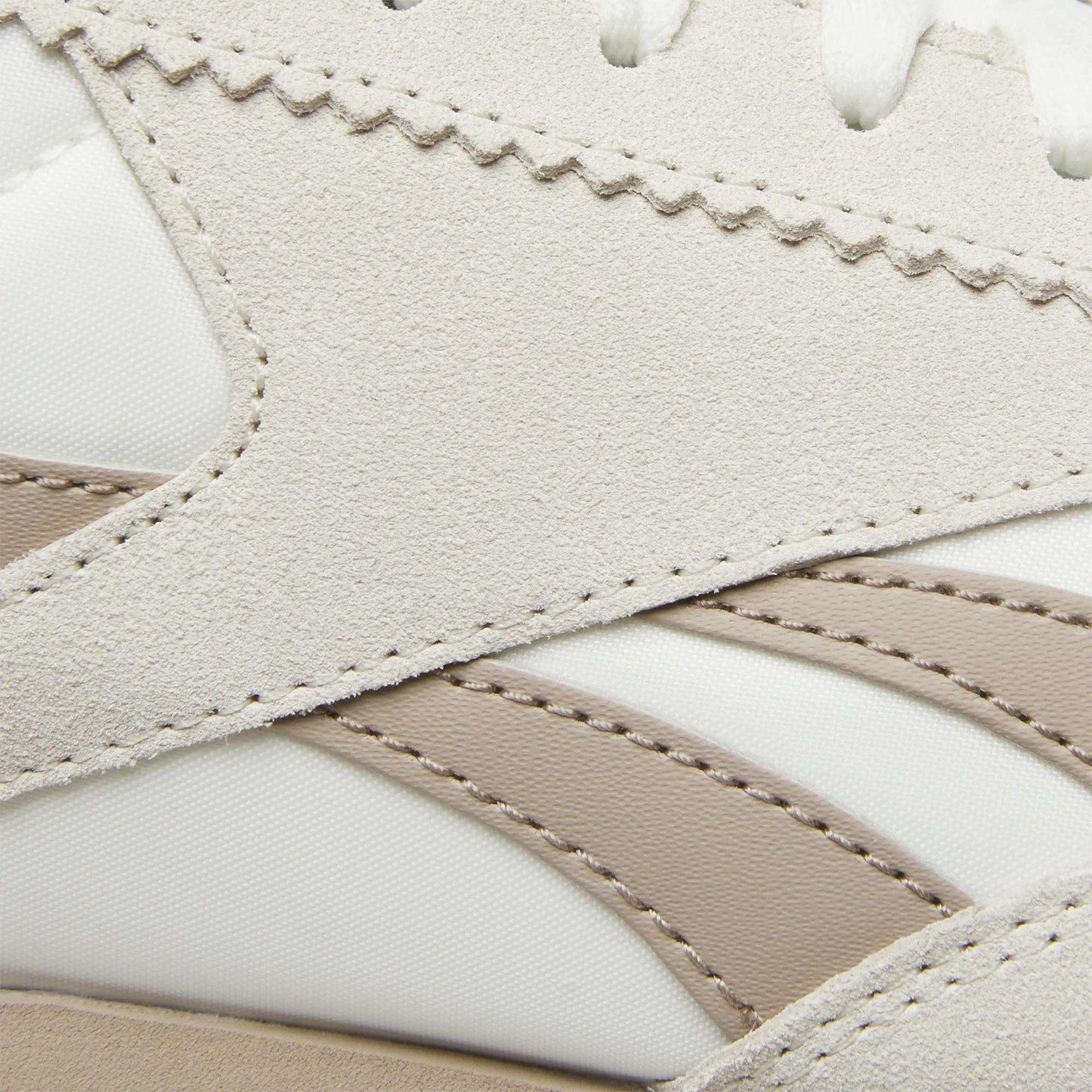Close-up of Reebok R100 Shoes highlighting beige suede overlays, white textile uppers, and taupe synthetic stripes with detailed stitching. These low-profile sneakers feature layered textures and wavy edges inspired by '70s running styles.
