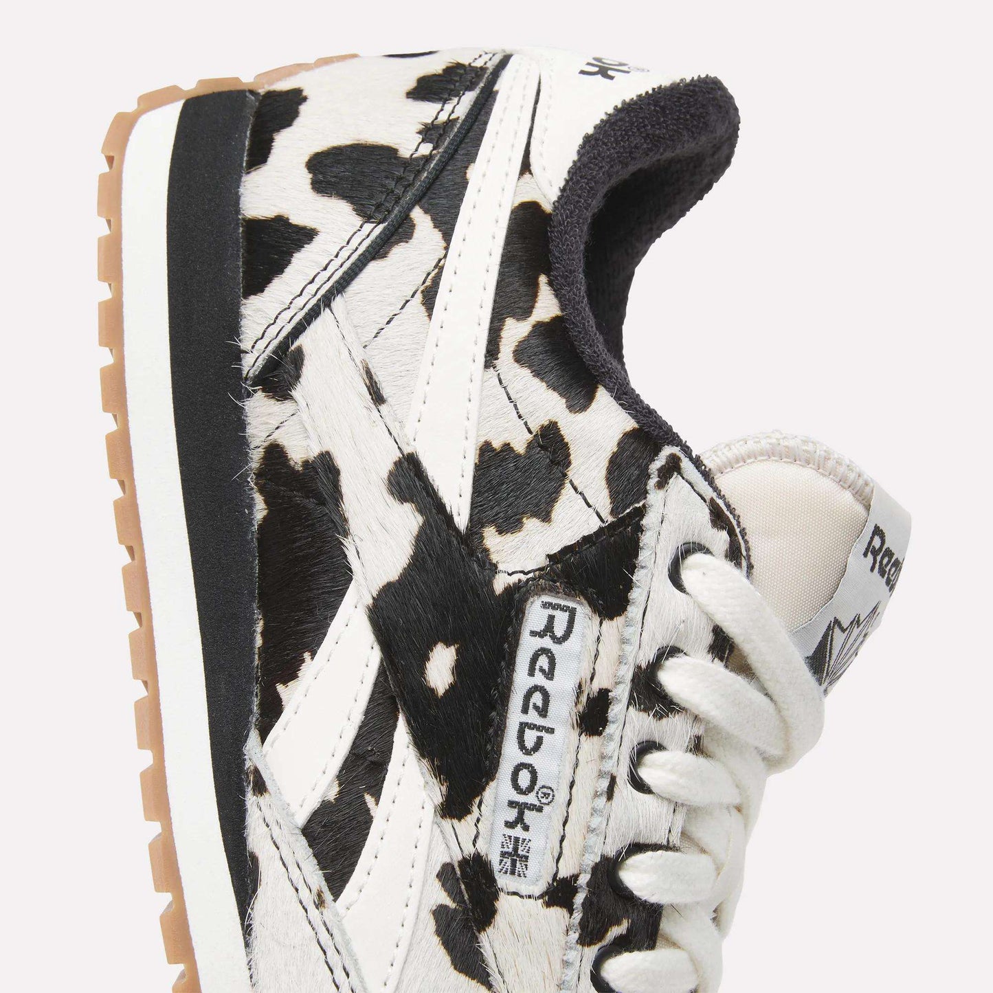 Close-up of Reebok Women's Classic AZ Shoes with a striking black and white animal print, white laces, beige sole, and prominent Reebok logo on the side and tongue.