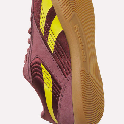 A close-up of Reebok Women's Ultra Lo Shoes in maroon with yellow stripes and a brown rubber sole, highlighting the side and bottom details against a white background.