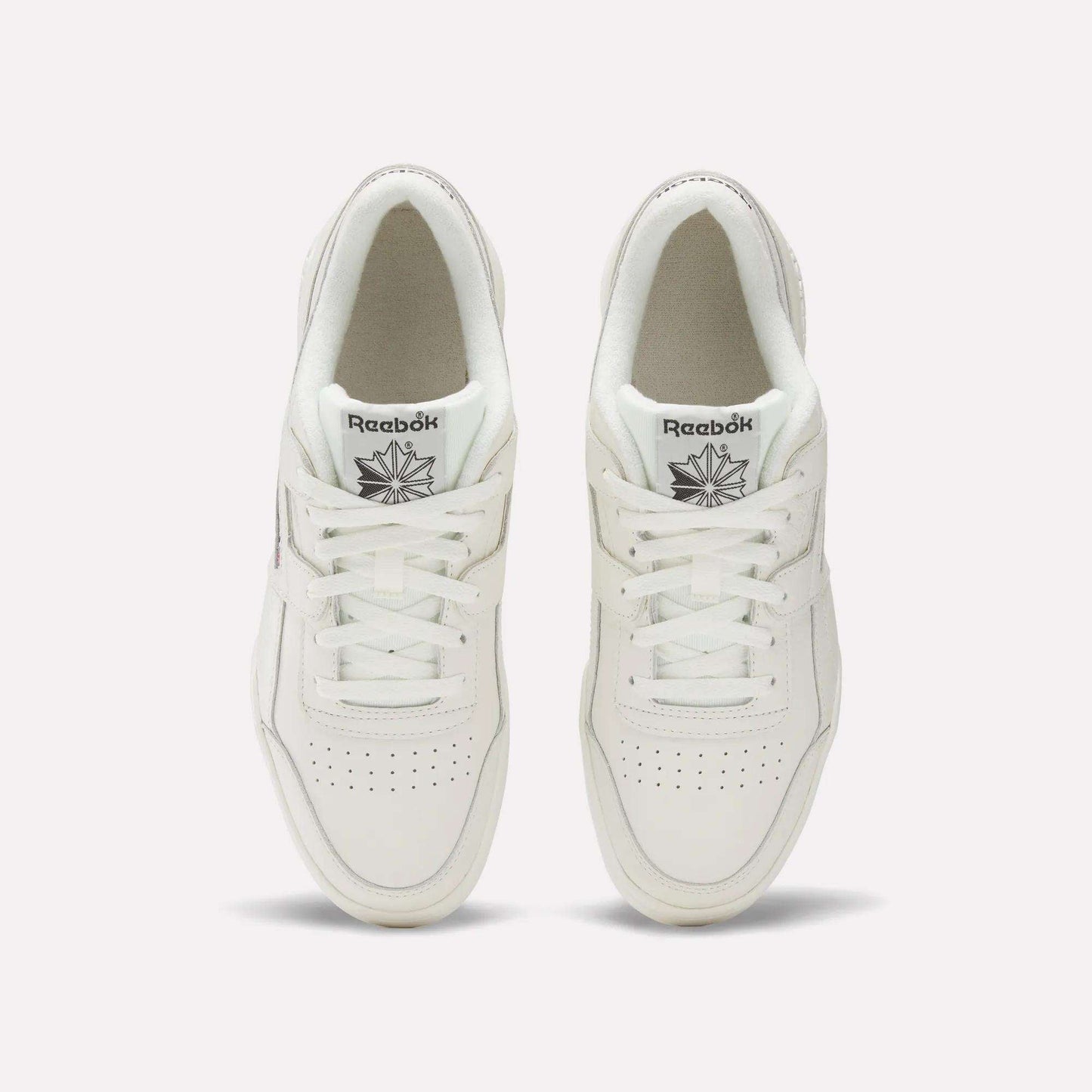 A pair of white Reebok Workout Plus Shoes viewed from above showcases classic '80s fitness style. The tops, laces, and Reebok logo on each tongue are visible, set against a plain light background.