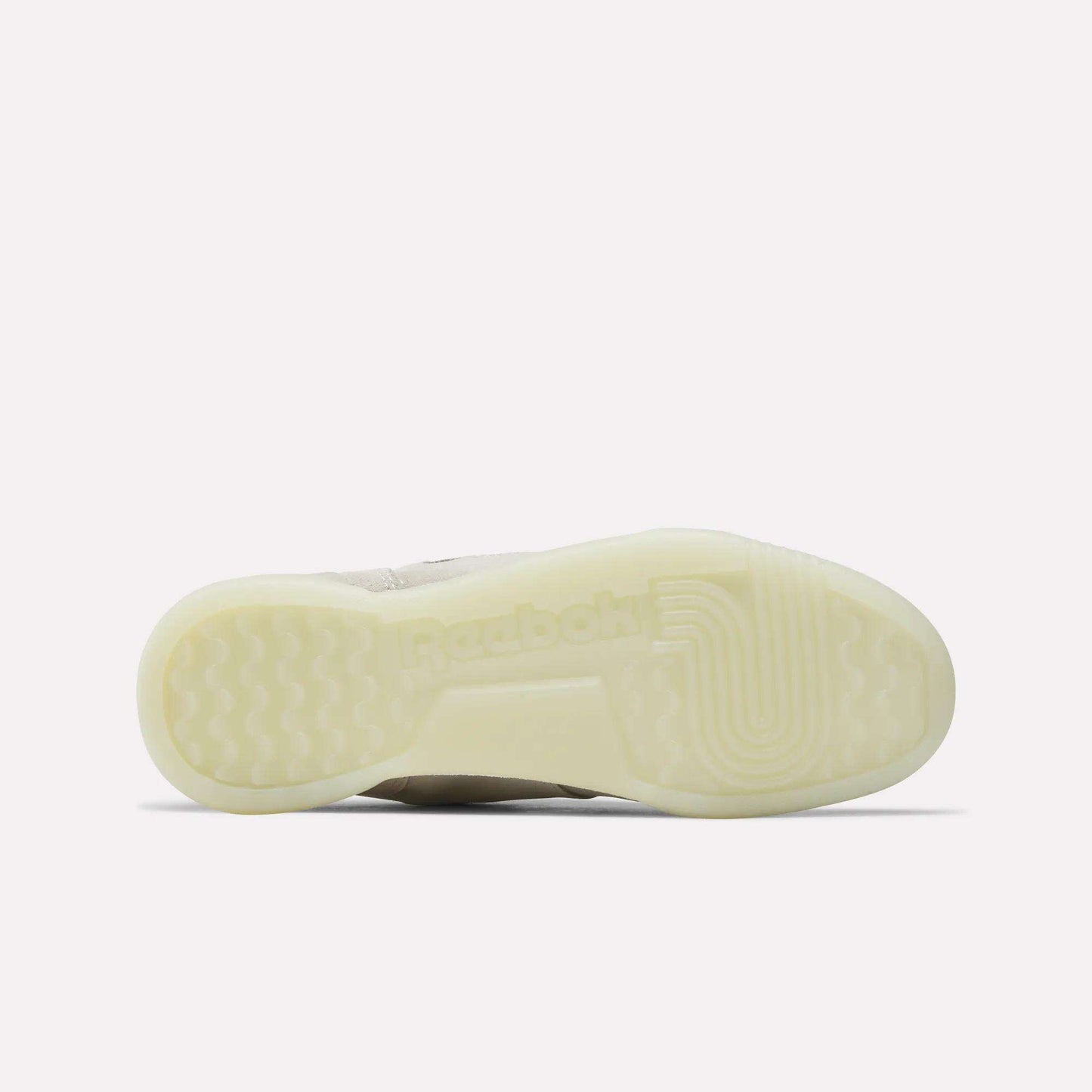 The image shows the translucent sole of the Reebok Women's Workout Plus Shoes, viewed from beneath, featuring the Reebok logo and textured grip patterns inspired by classic '80s fitness style.