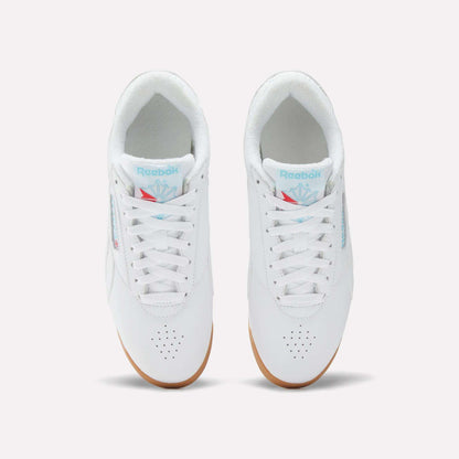 Top view of Reebok Women's Freestyle Lo Shoes in white with white laces, light blue branding on the tongue, perforated toe area, and light brown gum soles, set against a plain white background.