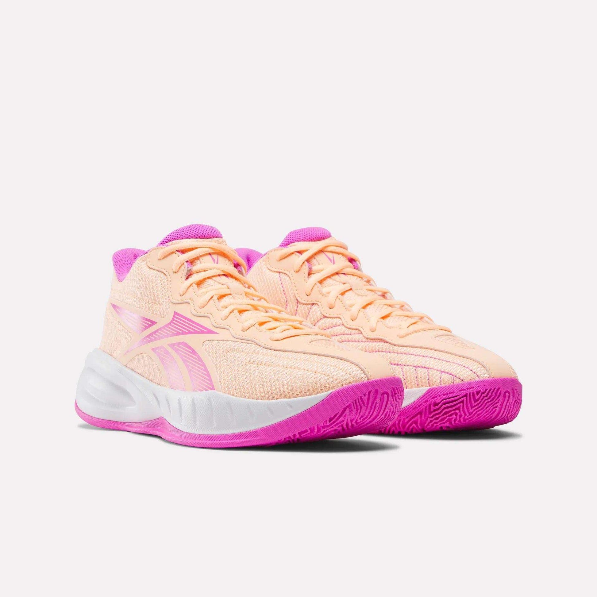 A pair of peach Press Basketball Shoes by Reebok with bright pink accents on the tongue, sole, and logo, featuring EVA cushioning for soft, responsive comfort—all shown against a plain white background.