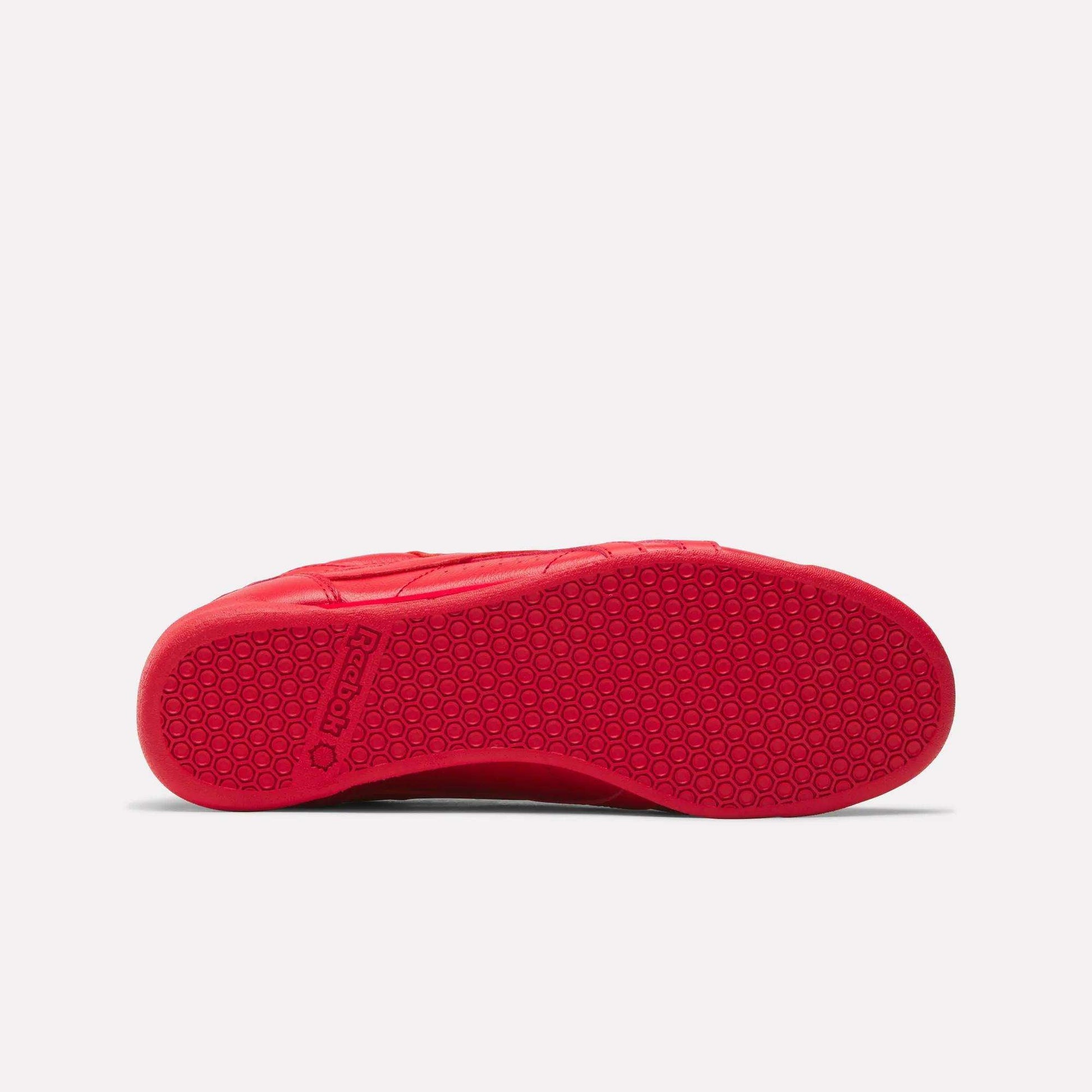 Red Women's Freestyle Lo Shoes from Reebok shown from the bottom, featuring a textured rubber sole with a hexagonal pattern and the Reebok logo near the heel. Perfect addition to any women's shoe collection. White background.
